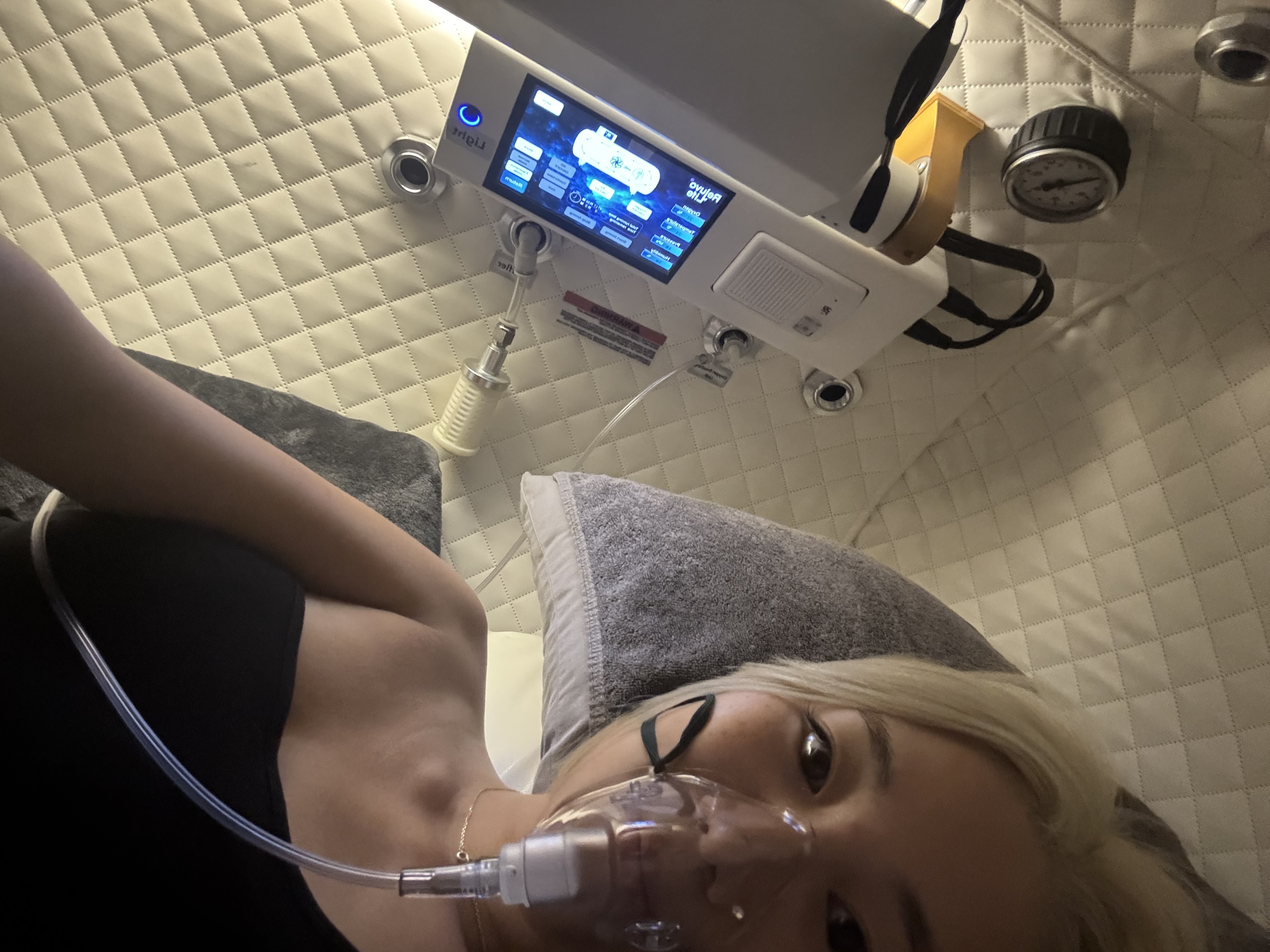 Cathy inside a hyperbaric oxygen chamber, oxygen mask on, control panel visible above